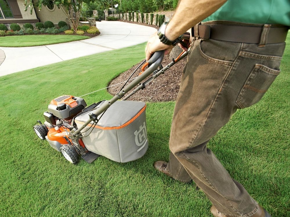 A lawn care professional mowing a neatly maintained residential lawn.